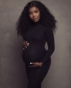 a pregnant woman posing for the camera with her hands on her stomach and wearing a black dress