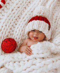 a baby wearing a santa hat and laying on a blanket with a red ornament