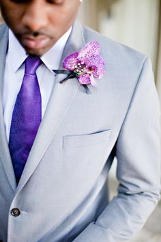 a man in a gray suit with a purple tie and flower boutonniere