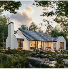 a white house surrounded by rocks and trees with a river running through the front yard