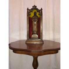 a small wooden table with a statue on it's top and a curtain behind it