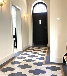 a hallway with black and white tiles on the floor next to a wooden bench in front of a door