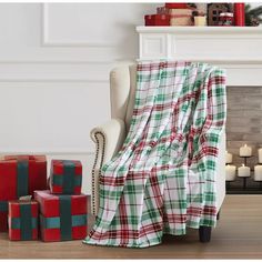 a plaid blanket sitting on top of a white chair next to christmas presents in front of a fireplace