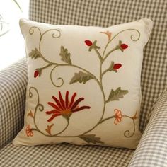 a white pillow with red flowers on it sitting on a checkered chair in front of a window