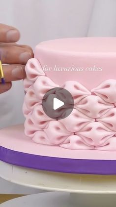 a person is decorating a pink cake with purple icing and a gold pen