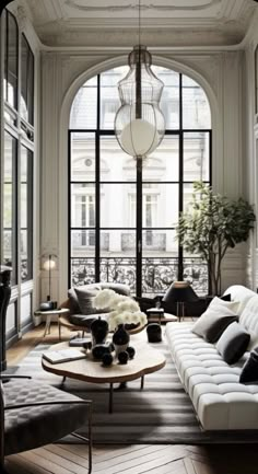 a living room filled with lots of furniture next to large windows and a chandelier hanging from the ceiling