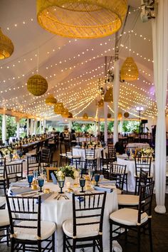 tables and chairs are set up in a tent with lights hanging from the ceiling above them