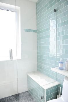 a white toilet sitting next to a bath tub in a bathroom with blue tiles on the walls