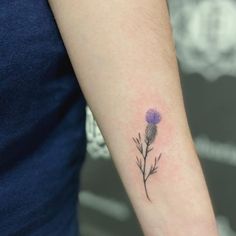 a small purple flower tattoo on the arm