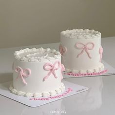 two white cakes with pink bows on them sitting on top of a table next to each other