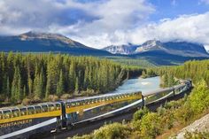 a train traveling down tracks next to a forest filled mountain range with trees and mountains in the background