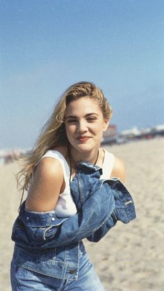 a woman standing on top of a sandy beach next to the ocean with her hair blowing in the wind