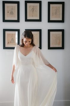 a woman in a white dress standing next to some framed pictures and holding her hand on her hip