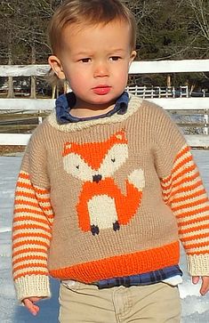 a little boy standing in the snow wearing a sweater with a fox on it