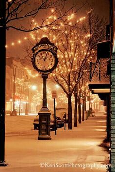 a clock sitting on the side of a road covered in snow next to street lights