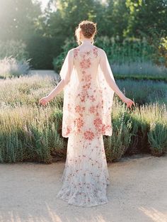 a woman standing in front of lavender bushes wearing a white dress with pink flowers on it