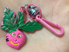 a pink keychain with a green leafy design on it and a metal bell in the shape of a head