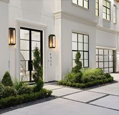 a large white building with two black doors and windows on each side, surrounded by greenery