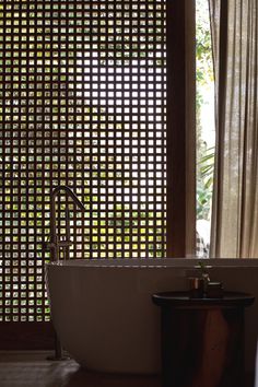 a bath tub sitting next to a window covered in sheered curtains and a wooden table