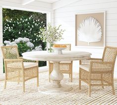 a dining room table with chairs and a vase on the table in front of an open window