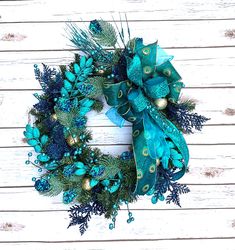 a wreath with blue and green decorations hanging on a white wooden wall in front of a door