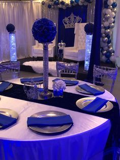 a table set up for a party with blue and silver decorations on the tables, chairs and centerpieces