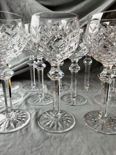 six crystal wine glasses sitting on top of a tablecloth covered table with silver cloth