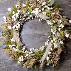 a wreath with white flowers and green leaves on a wooden floor in front of a wall