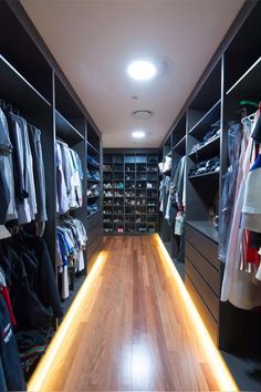 a walk - in closet with lots of clothes on the shelves and wooden flooring