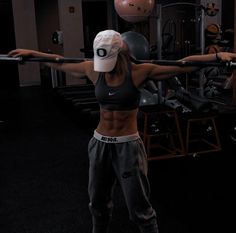 a woman is doing exercises with a barbell in the gym while wearing a hat