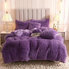 a bed with purple comforter and pillows on top of it in a room next to two lamps