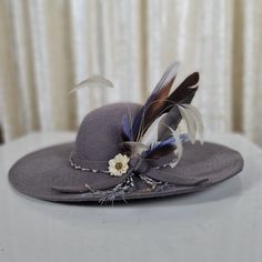 This grey floppy wide-brimmed fedora hat is made of 100% pure wool felt with grey and white braid and blue, grey and white feather decoration. It's an elegant and unusual design that will surely turn heads.  It looks so good and is so lovely to wear that you won't want to take it off.  Hat size is 57cm. Gray Brimmed Fedora For Spring, Gray Short Brim Fedora For Spring, Elegant Gray Wide Brim Felt Hat, Gray Brimmed Hat For Kentucky Derby, Gray Curved Brim Hat For Kentucky Derby, Adjustable Brimmed Gray Felt Hat, Adjustable Gray Brimmed Felt Hat, Gray Short Brim Hat For Kentucky Derby, Gray Wide Brim Felt Hat With Adjustable Fit