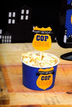 a blue cup filled with popcorn sitting on top of a wooden table next to a computer