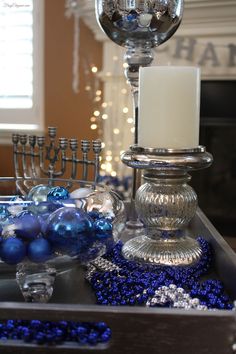 a silver tray with blue ornaments and candles on it in front of a lit candle