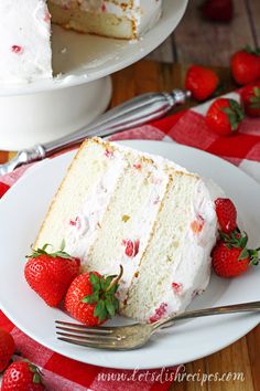 a slice of cake with white frosting and strawberries on the plate next to it