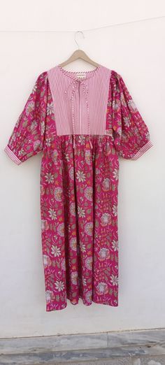 a pink and white floral dress hanging on a clothes hanger against a white wall