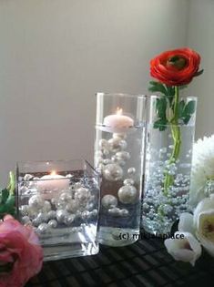 three glass vases with candles and flowers in them sitting on a table next to each other