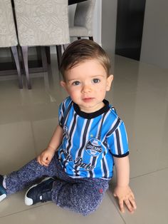 a little boy sitting on the floor with his legs crossed and looking at the camera