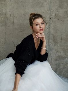 a woman is sitting on the floor wearing a white skirt and black sweater with pearls