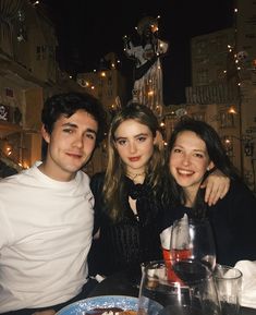 three people sitting at a table with food and drinks in front of them, posing for the camera