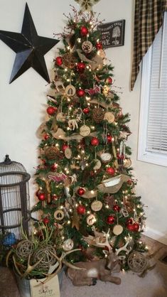 a christmas tree with ornaments on it in front of a birdcage and window