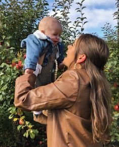 a woman holding a baby up to her face in an apple tree filled with apples