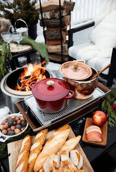 a table with bread, apples and other food on it in front of an outdoor fire pit