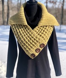 a yellow knitted cowl with buttons on the collar is sitting on a black mannequin