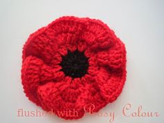 a crocheted red flower with black center sits on a white surface, ready to be used as a brooch