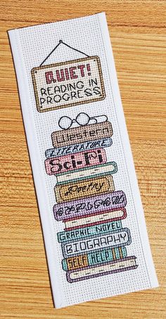 a cross stitch bookmark with the words quiet reading in progress written on it, sitting on a wooden surface