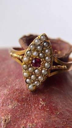 A beautiful antique Victorian navette ring featuring a natural ruby surrounded by beautiful seed pearls. The ruby takes centre stage - a pigeon red pop of colour that has such a presence for its size! It is bright, strong and powerful! Surrounding the ruby are 21 creamy grey, seed pearls, all original, in a beautiful navette form. What I particularly like is the sweet gold detailing in between each seed pearl and the patina is so wonderful, an old matt yellow gold. With beautiful detailed split Vintage Marquise Ruby Ring Gift, Vintage Marquise Ruby Ring As Gift, Vintage Marquise Ruby Ring For Gift, Vintage Marquise Ruby Ring In Red, Vintage Marquise Ruby Wedding Ring, Shaena Targaryen, Ruby And Pearl Ring, Navette Ring, Ruby And Pearl