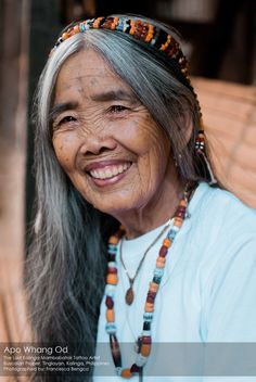 an old woman with long gray hair and beaded headdress smiles at the camera