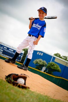 a young boy holding a baseball bat standing on top of a dirt field next to a catchers mitt