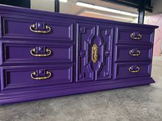 a purple dresser with gold handles and knobs on the doors is in an empty room